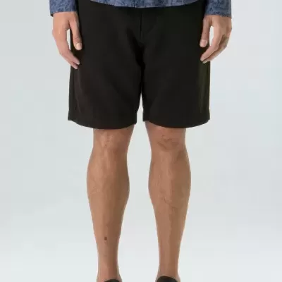 Homem de pé com calções pretos, camisa azul com padrão e ténis pretos