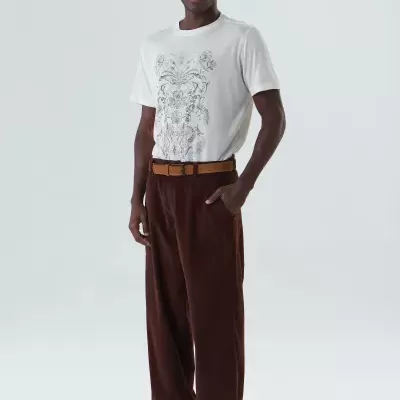 Homem vestido com t-shirt branca estampada, calças castanhas, cinto castanho e sapatos pretos