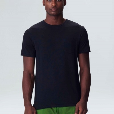 Homem com t-shirt preta e calças verdes em fundo cinza claro