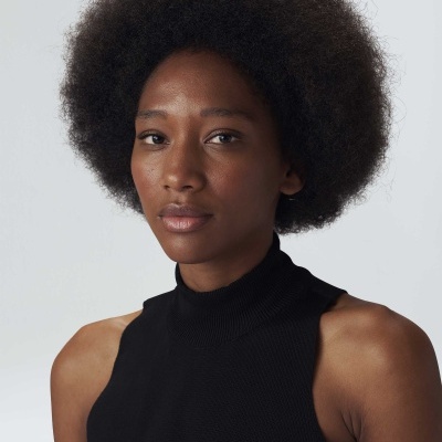 Mulher com camisola preta sem mangas e cabelo afro contra fundo cinza claro