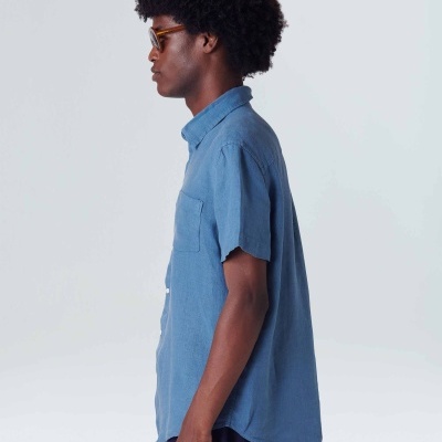 Homem de perfil com camisa azul de manga curta e óculos, fundo branco