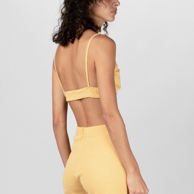 Mulher de costas com top e calças amarelas sobre fundo cinza