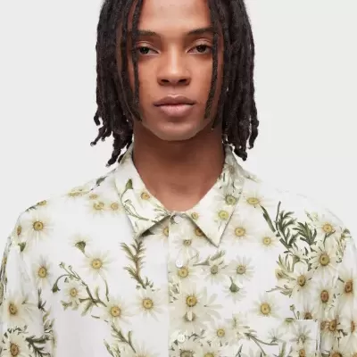 Camisa branca com padrão floral amarelo e verde usada por modelo com cabelo dreadlocks