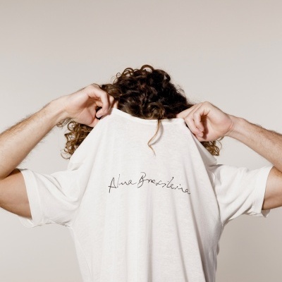 Camiseta branca de algodão com texto Alama Brasileira na parte de trás usada por pessoa de cabelo encaracolado