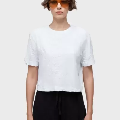 Mulher a usar t-shirt branca enrugada, calção preto e óculos de sol castanhos