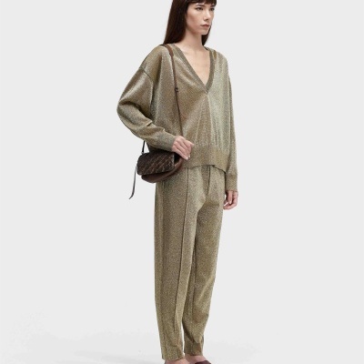 Mulher a usar conjunto dourado de calças e camisola com sandálias e mala castanhas.