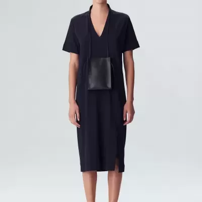 Mulher com vestido preto de manga curta e bolsa preta pequena pendurada ao pescoço