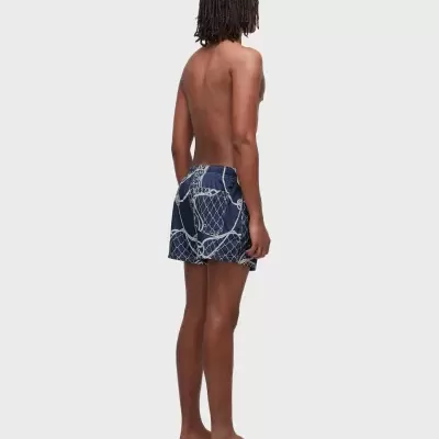 Homem de costas a usar shorts de banho azuis com padrão de cordas brancas e sandálias bege