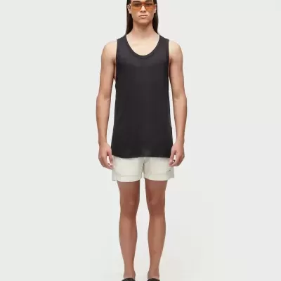 Homem de pé com regata preta, calções brancos e chinelos pretos trançados