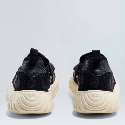 Sapatilhas pretas com solado bege vistas de trás sobre fundo cinzento