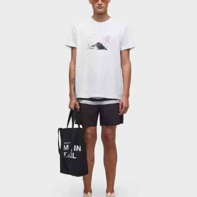 Homem com t-shirt branca e calções pretos segurando bolsa preta com texto em fundo branco.
