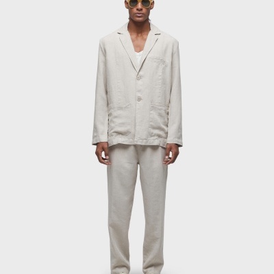 Homem vestido com fato bege claro, ténis bege e óculos de sol amarelos em fundo branco