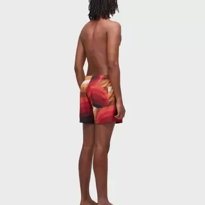 Homem de costas de calções de banho com padrão colorido e sandálias castanhas.