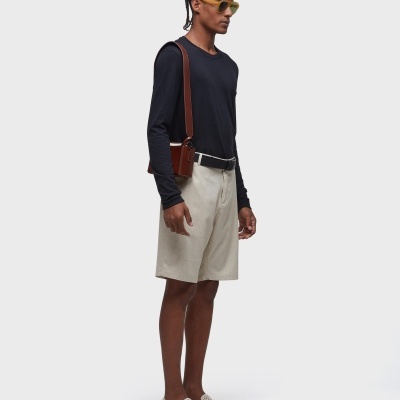 Homem com camisola preta, calções bege, sapatos bege perfurados, óculos amarelos e bolsa castanha.