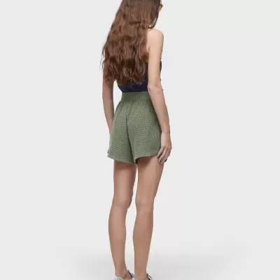 Mulher vista de costas a usar shorts verdes xadrez, top azul escuro e ténis brancos