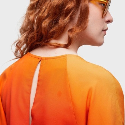 Mulher de perfil de cabelo ruivo com blusa laranja e amarelo, óculos amarelos