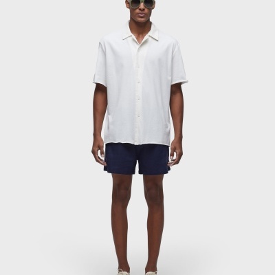 Homem com camisa branca, calções azuis escuros e óculos de sol