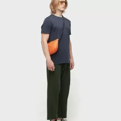 Homem com t-shirt azul, calças verde-escuras, ténis pretos e mochila pequena laranja