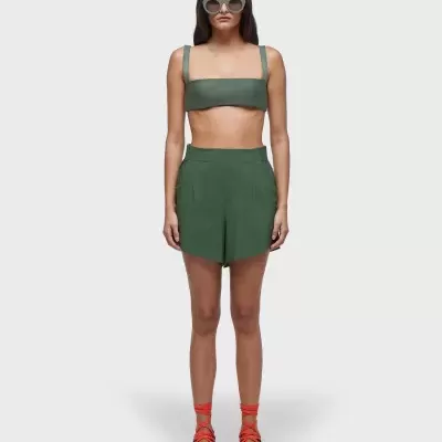 Mulher com conjunto desportivo verde, óculos de sol cinzentos, meias vermelhas e sapatos cinzentos