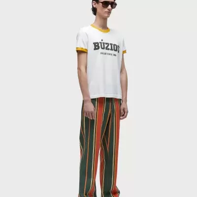 Pessoa com t-shirt branca BÚZIOS e calças às riscas verticais coloridas em fundo branco.
