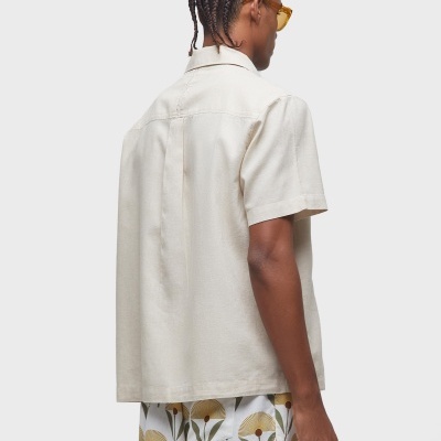 Homem de costas com camisa bege de manga curta e calções florais brancos.