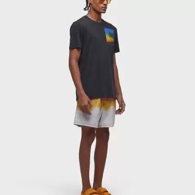 Homem com t-shirt preta, calções cinza e ténis alaranjados num fundo branco