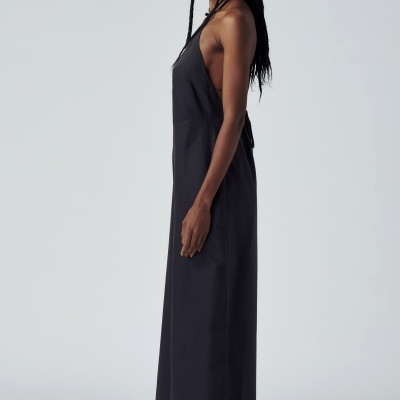 Vestido comprido preto sem mangas com decote assimétrico usado por modelo feminina com óculos escuros e sandálias castanhas