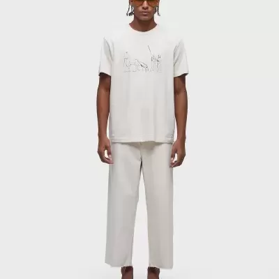 Homem a usar t-shirt clara com estampa minimalista e calças largas, sandálias castanhas e óculos de sol.