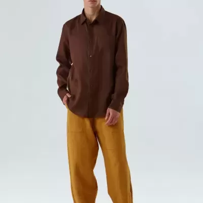 Homem com camisa castanha e calças largas castanhas claras em fundo branco