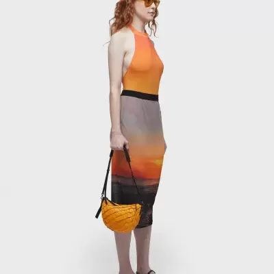 Mulher com vestido midi alaranjado degradê, óculos laranja, sandálias pretas e bolsa amarela trançada