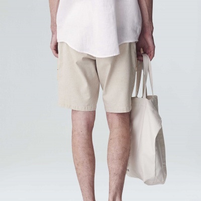 Homem visto de costas com calções bege, camisa branca, sapatos castanhos e mala creme.