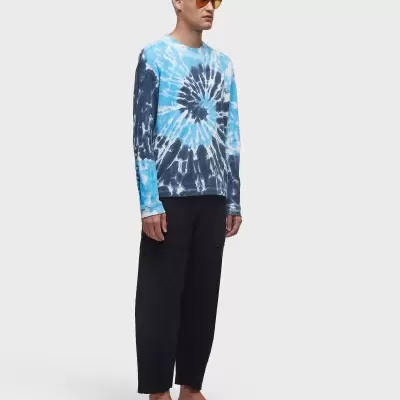 Homem com camisola tie-dye azul e calças pretas, óculos de sol e sandálias