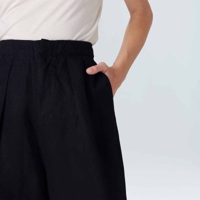 Pessoa com calças pretas largas e camisola branca, mão no bolso