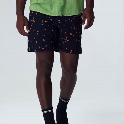 homem a usar camisa verde, calções pretos com flores laranjas e sapatos pretos