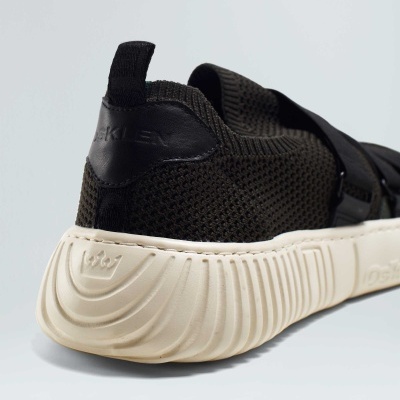 Ténis desportivo preto com sola branca texturizada sobre fundo cinza claro