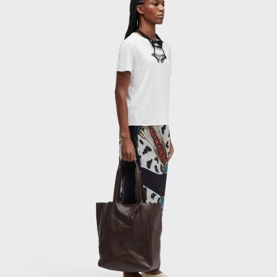 Modelo vestindo camisola branca com borboleta, saia colorida, sapatos brancos e saco de pele castanho