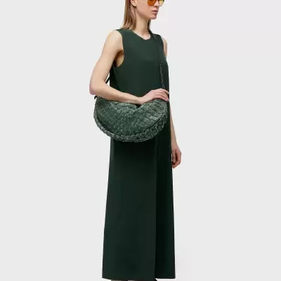 Mulher com vestido verde, bolsa trançada verde e ténis castanhos