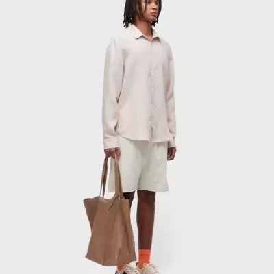 Pessoa vestindo camisa bege, calções brancos e segurando uma bolsa de couro castanha