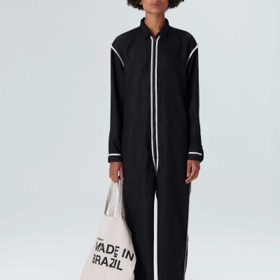 Mulher com macacão preto e saco de tecido branco com texto MAE IN BRAZIL