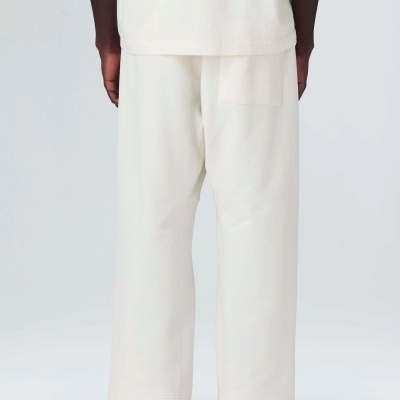 Pessoa de costas com calças e camisola brancas, calçado branco, fundo claro