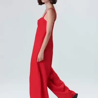 Macacão vermelho feminino com alças finas e pernas largas, chapéu de palha bege e sandálias pretas