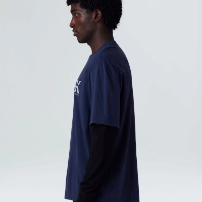 Homem de perfil com t-shirt azul escura e camisa preta de manga comprida.