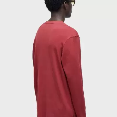 Pessoa de costas a usar camisola de manga comprida cor de tijolo sobre calças castanhas com faixa azul clara