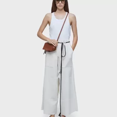 Mulher com roupa branca e acessórios marrons em fundo branco