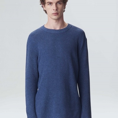 Homem com camisola de malha azul e calças azuis, fundo neutro.