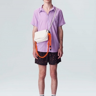 Homem vestindo camisa roxa, calções pretos com padrão laranja e bolsa branca com cordão laranja