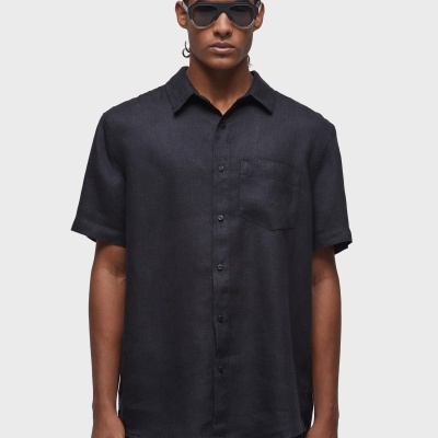 Camisa preta de manga curta com bolso, botões e gola clássica vestida por modelo de óculos escuros