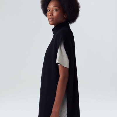 Mulher vestindo colete negro longo com gola alta sobre vestido cinzento de malha