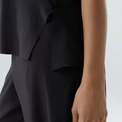 Pessoa com roupa preta, calças e blusa com corte assimétrico, fundo claro