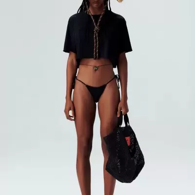 Mulher a vestir biquíni preto, t-shirt preta, chapéu de palha e mochila preta